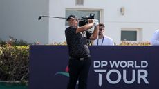 Patrick Reed holds his finish on a tee shot in front of a navy blue DP World Tour sign