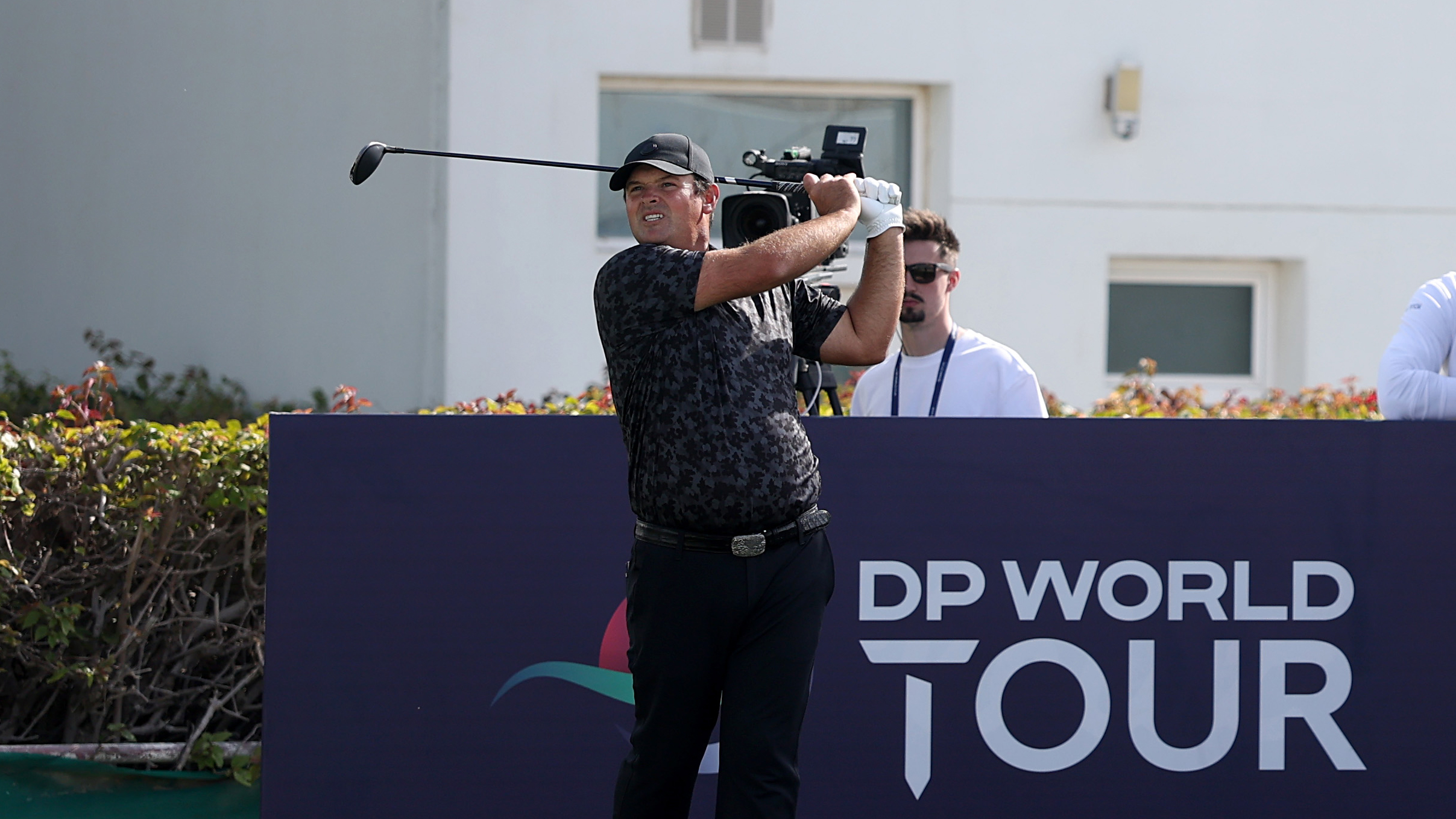Patrick Reed holds his finish on a tee shot in front of a navy blue DP World Tour sign