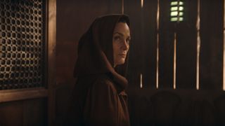 A hooded Indara sees someone off camera while she sits in a diner in Star Wars: The Acolyte