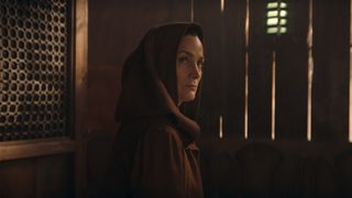 Une Indara encapuchonnée voit quelqu'un hors champ alors qu'elle est assise dans un restaurant dans Star Wars : The Acolyte.