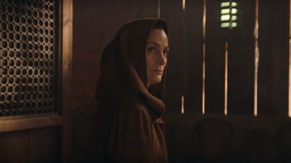 A hooded Indara sees someone off camera while she sits in a diner in Star Wars: The Acolyte