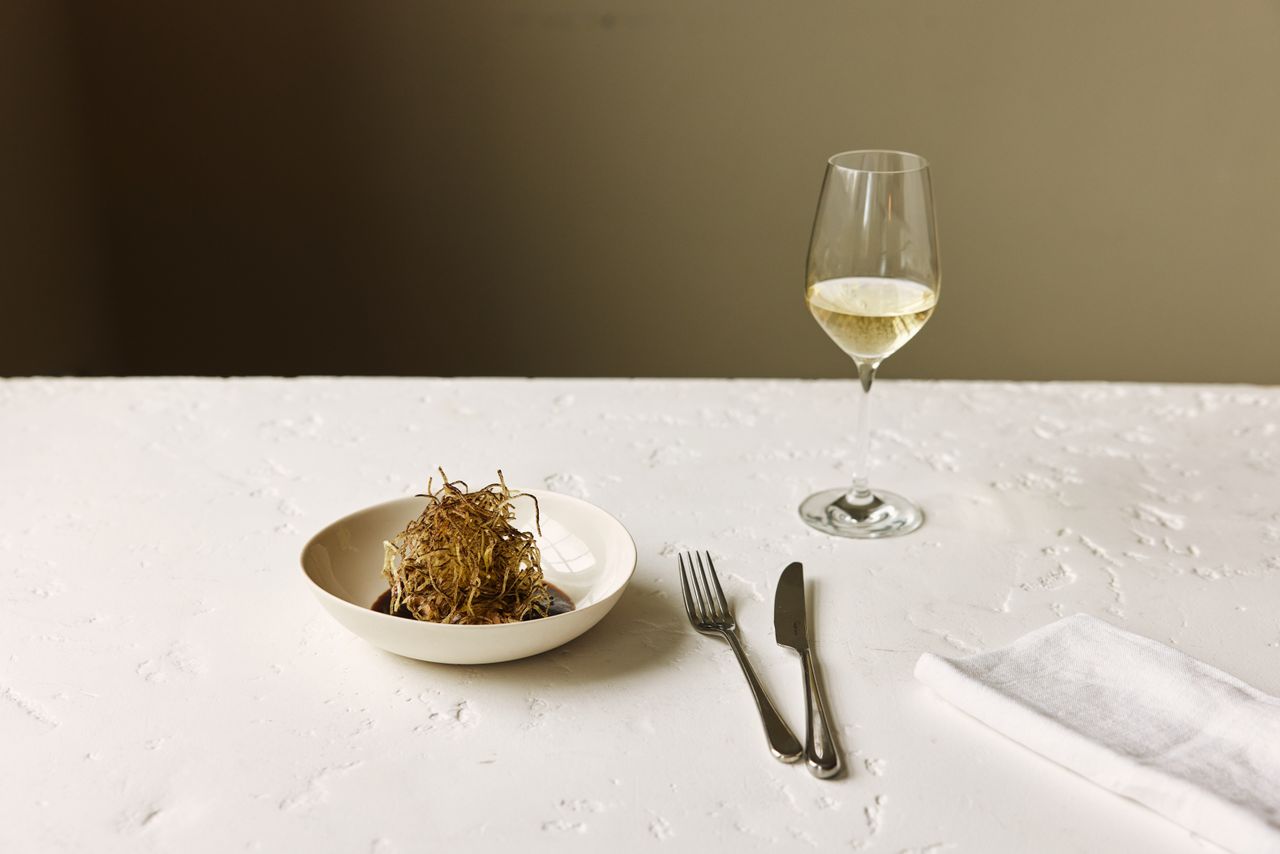 A plant-based restaurant's dishes feature greens and vegan ingredients assembled into visually striking, earthy plates served in white dishes against textural surfaces.