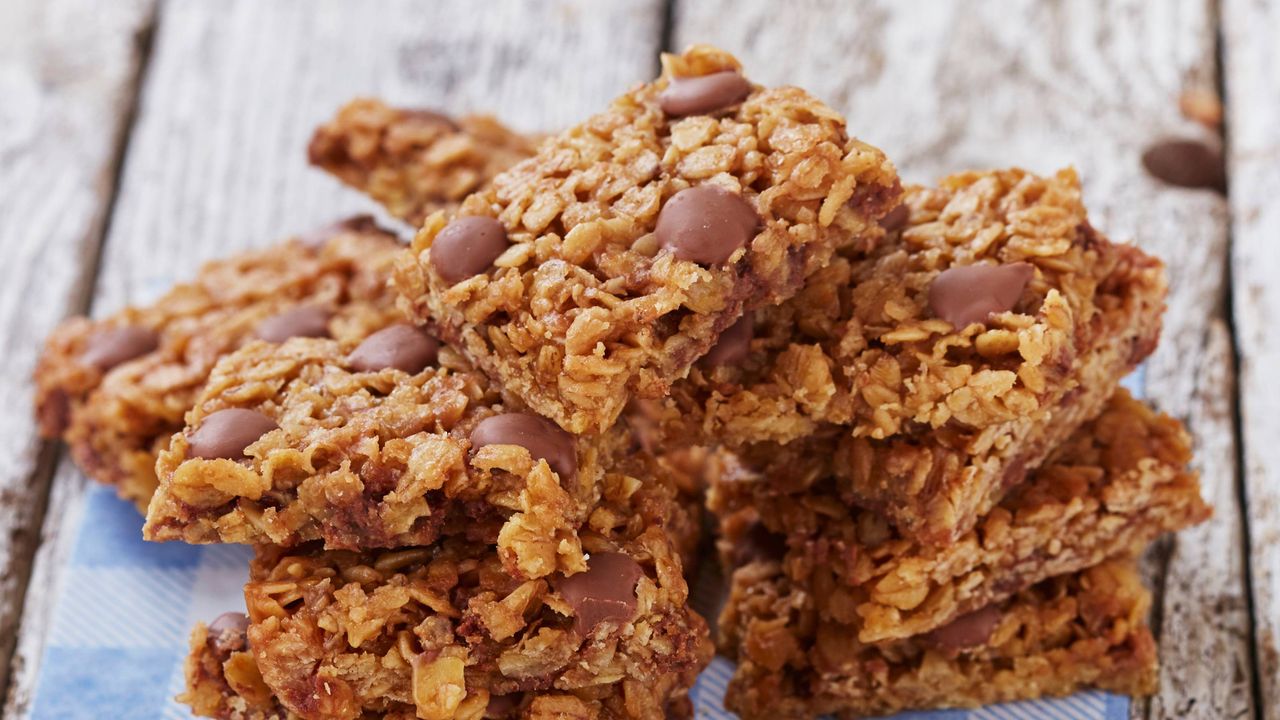 Chocolate chip flapjacks cut into squares and stacked on top of a blue check cloth