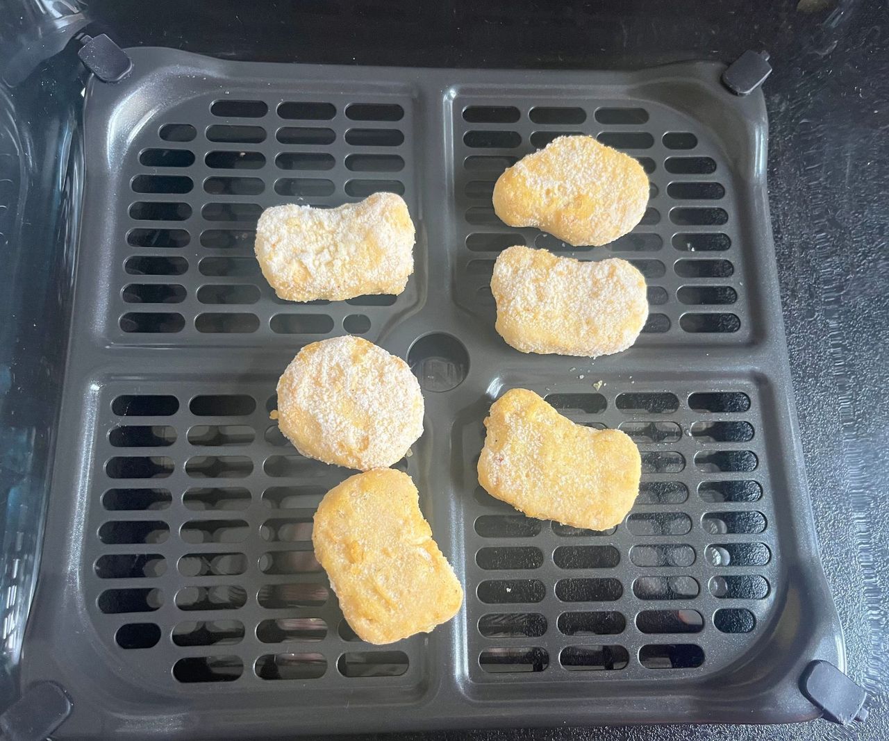 Six frozen nuggets on a black air dryer crisper tray