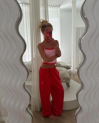 Emili Sindlev wears a pink camisole layered over a red camisole with red sweatpants.