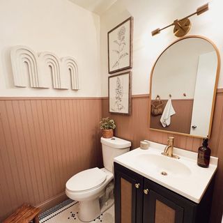 Small modern, cozy bathroom with painted half paneling in earthy hues, arched wall mirror, brass wall light, and arched decor on walls, with tiny bathroom floor tiles in mono pattern