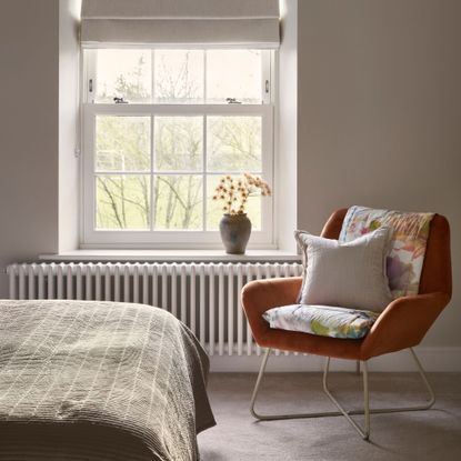 Bedroom with an orange accent chair sitting by the window, with a white radiator underneath it