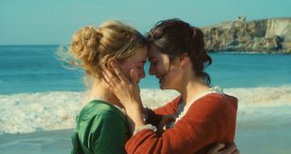 two women stand on the beach holding on to each other, their faces pressed together.