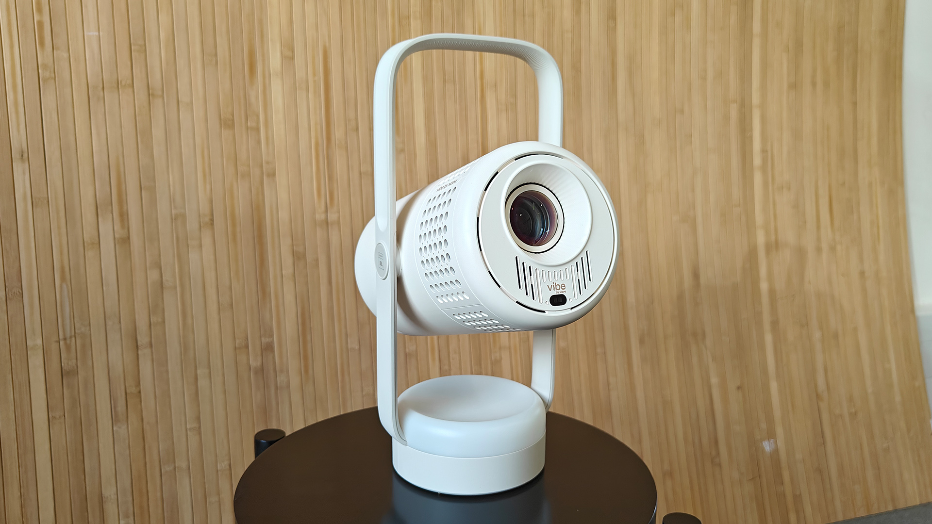 Xgimi Vibe One portable projector on small black table against bamboo effect wall