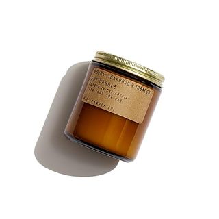 An amber glass jar with a ehite candle inside, a gold screw lid. A brown paper label with typewriting on it 