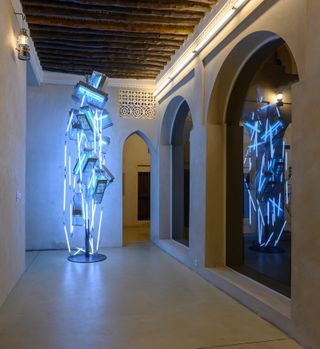 A futuristic light tall sculpture lit up with blue florescent lights, in a corridor-like space
