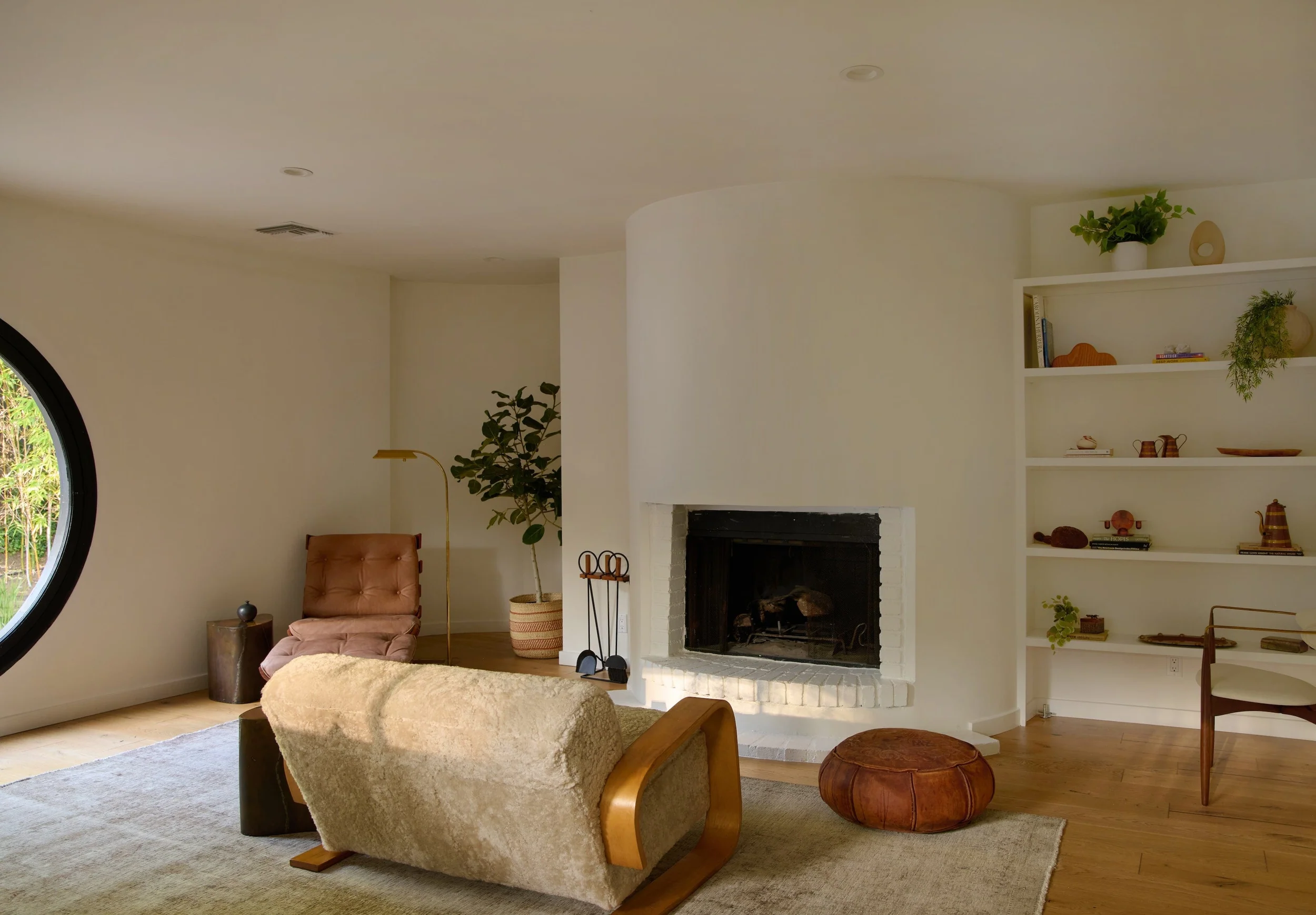 white walls with built in curved fireplace with white bricks, in front is a cream sheepskin lovseat with warm wood armrests