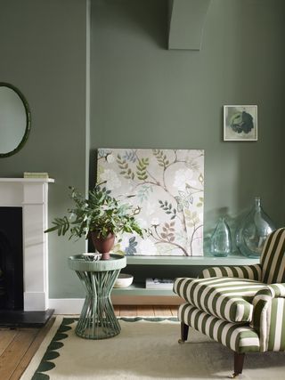 sage green wall in sitting room with green stripe chair and fireplace