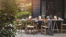 Outdoor dining area with wooden furniture decorated for a fall gathering with gray throws over the chairs and portable lamps along the table