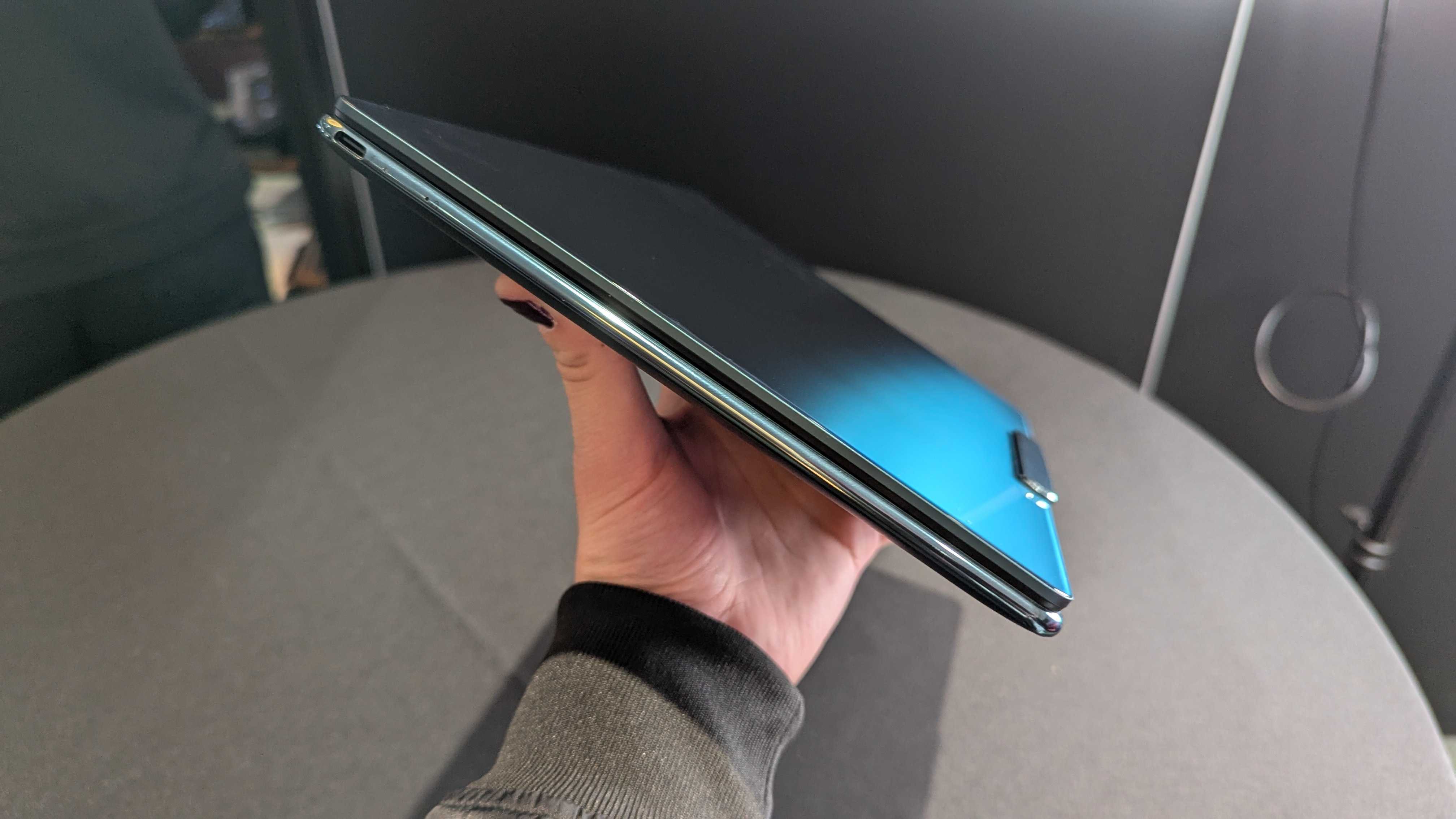 The Lenovo Yoga Slim 9i 14 (Gen 10) held in the hand, showing its curved edges and glossy lid.