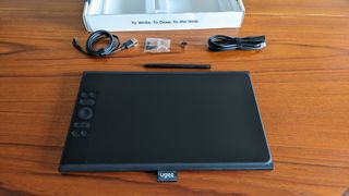Ugee UE12 Plus review; a drawing tablet on a wooden table with cables and a stylus