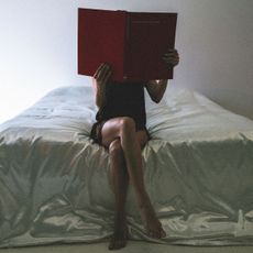 A woman reading a book in bed; bedsheets and flowers