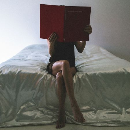 A woman reading a book in bed; bedsheets and flowers