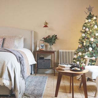 Beige bedroom with wooden floor, layered bedding, a wooden table and a christmas tree in the corner