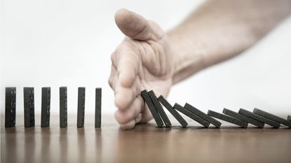 A man puts his hand between upright dominoes and dominoes that are falling.