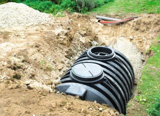 A black plastic septic tank partially concealed with soil