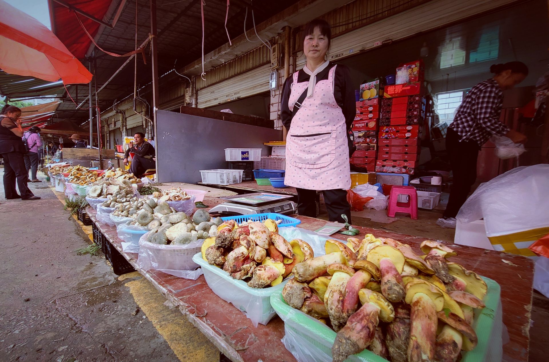 A woman stands behind bowls containing mushrooms.