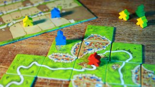 Carcassonne score board, tiles, and meeple laid out on a wooden table