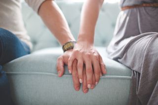 A couple with their hands place on top of each others on a sofa