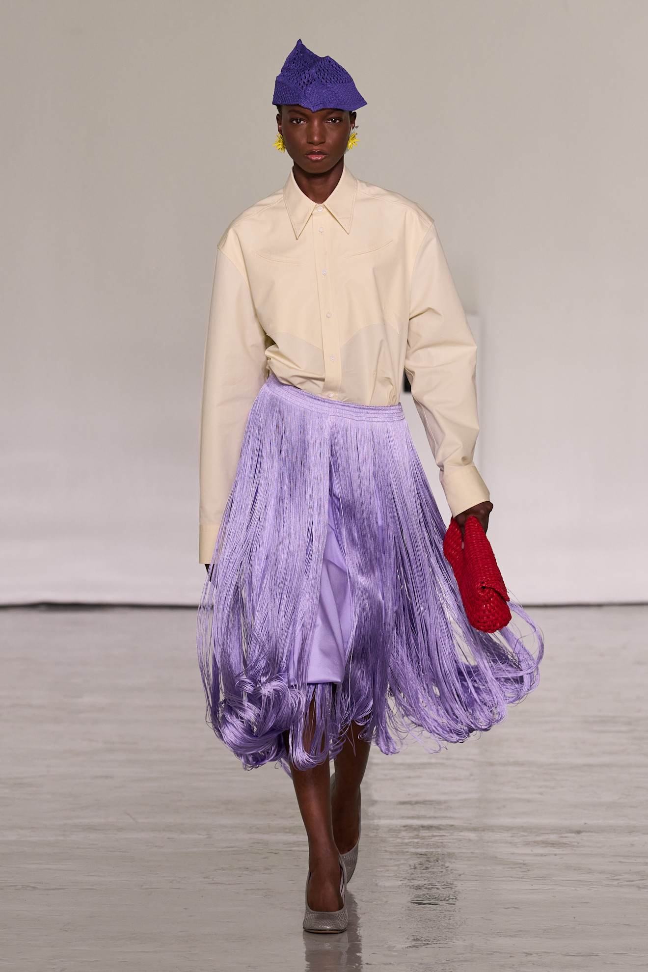 A model walks the runway at Bottega Veneta's spring/summer 2027 Milan Fashion Week show wearing a cream-colored button-down shirt with a purple fringe skirt.