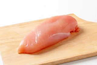 A raw chicken breast sits on a cutting board.