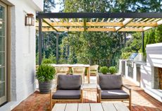 Patio with lounge area in the foreground, fireplace and built-in kitchen to the side, and dining set under a pergola at the back