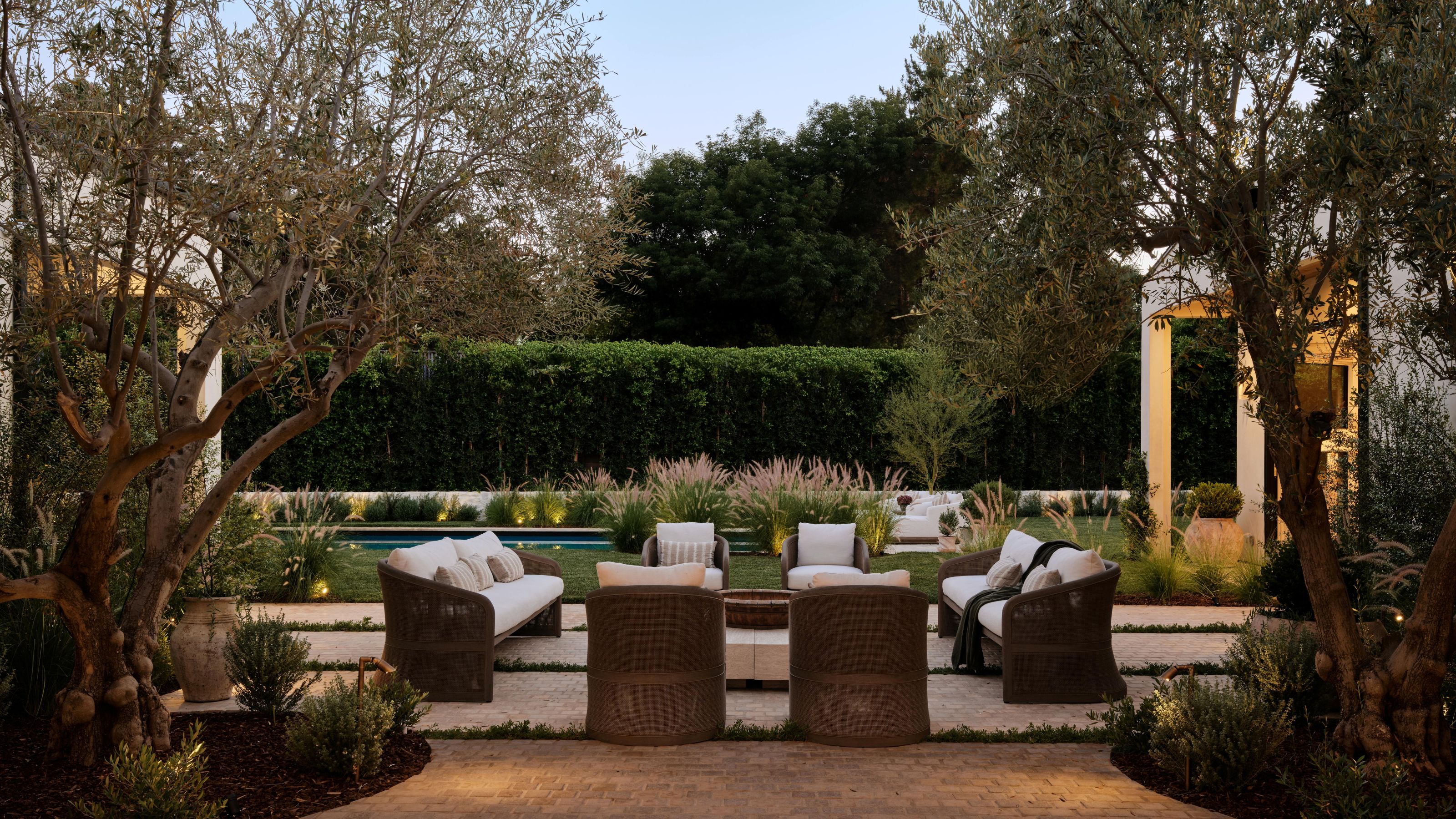 a large Mediterranean style patio area with rattan seating and large olive trees