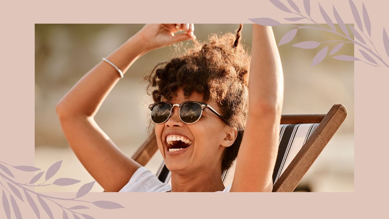 A woman in a deck chair wearing sunglasses and laughing in the sun for a guide on how to protect your hair from the sun