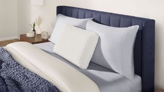 The Tempur-Pedic Temur-Cloud Pillow at the head of.a bed, resting upright in front of two other pillows that are propped against the headboard.