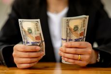 A businesswoman holds two stacks of $100 bills. One is much larger than the other.