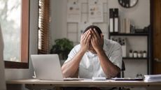 A man sitting at a desk has his head in his hands in frustration.