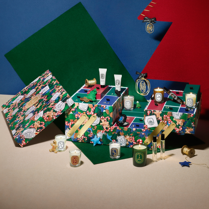 Lifestyle imagery of Diptyque Paris 2024 advent calendar set in front of red, green, blue christmas tree background