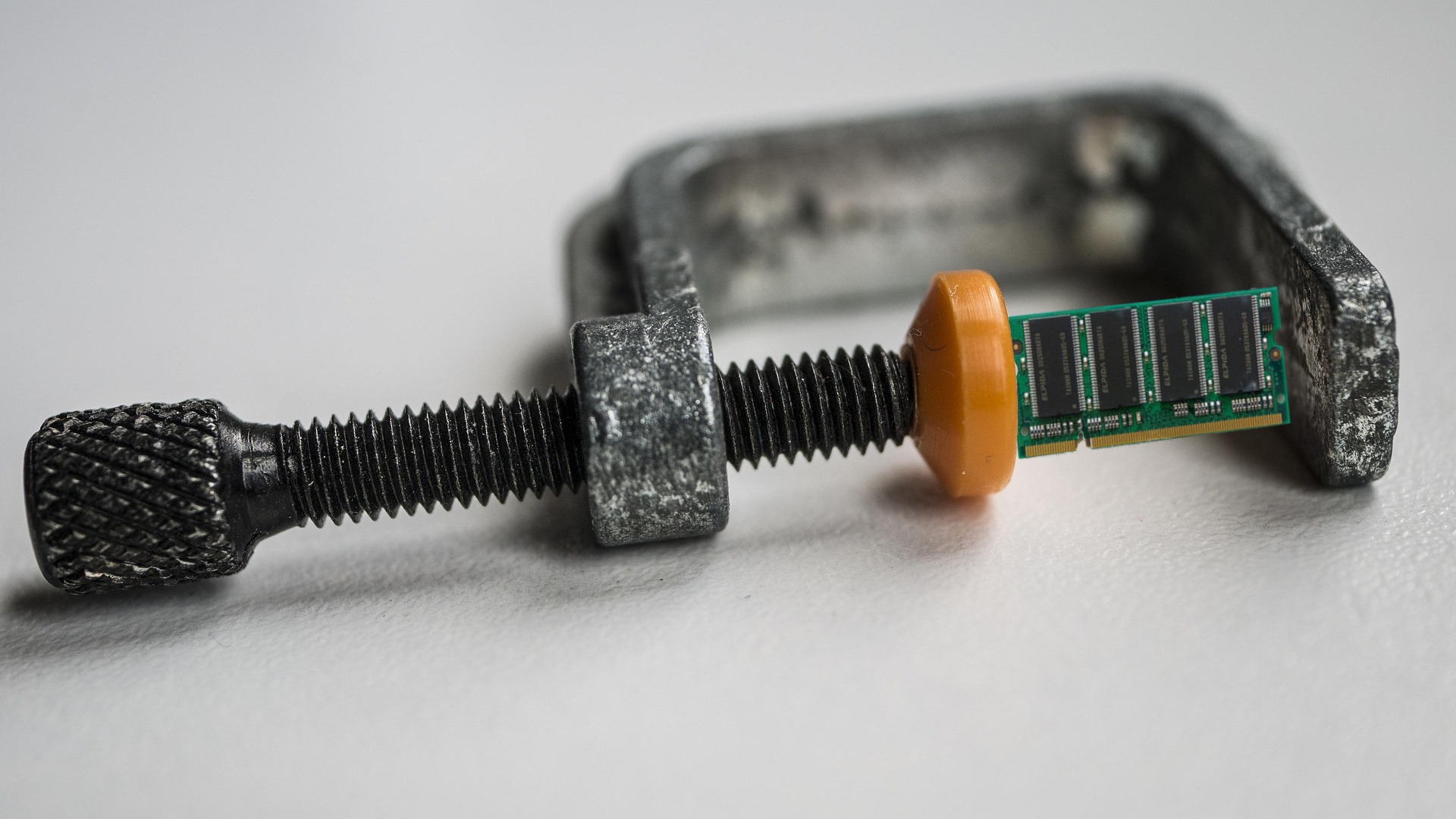 A manipulated photograph of a G-clamp holding a memory SO-DIMM.
