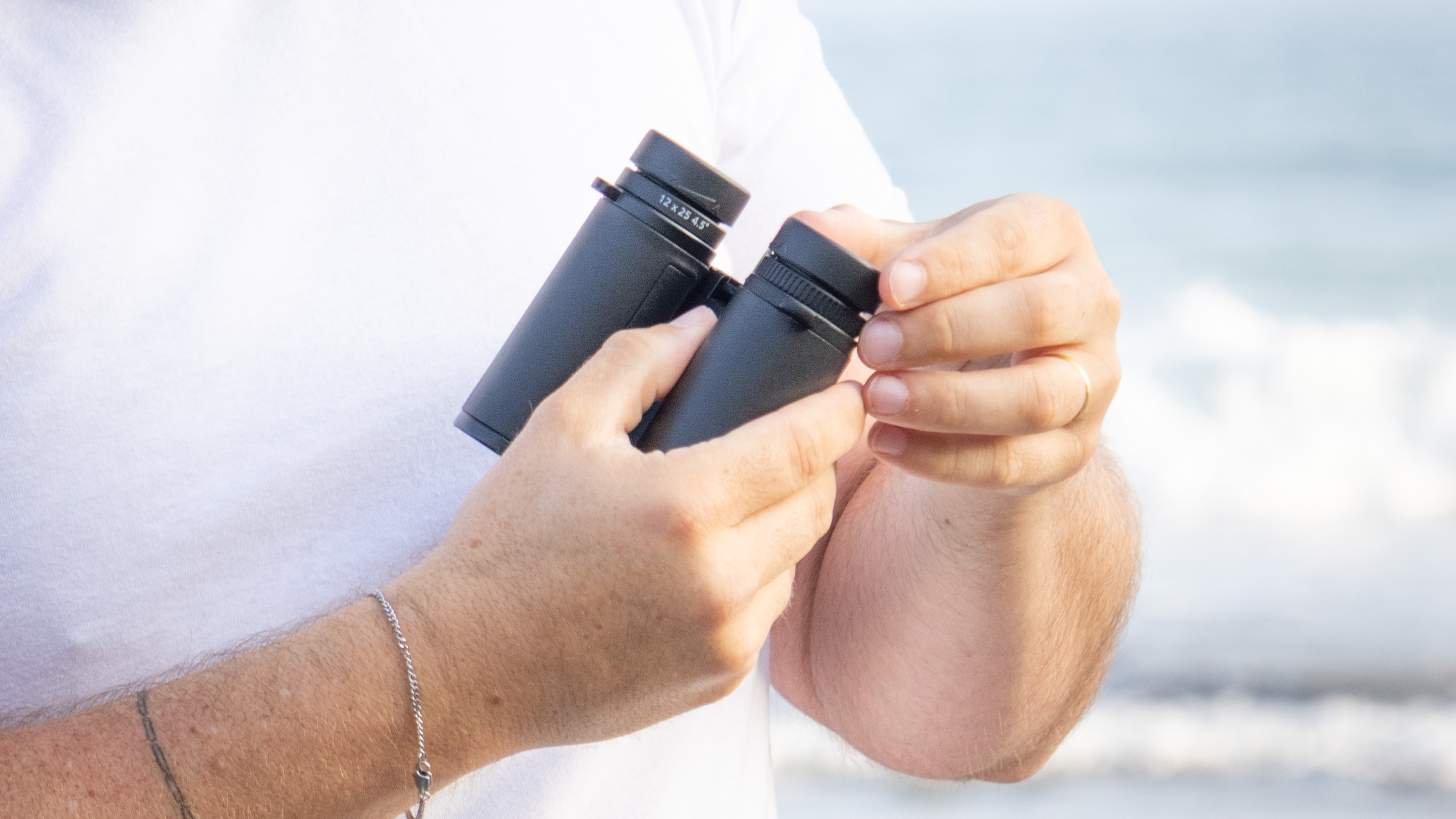 Nikon Stabilized 12x25 S binoculars held in the hands of the reviewer in front of breaking waves at the beach
