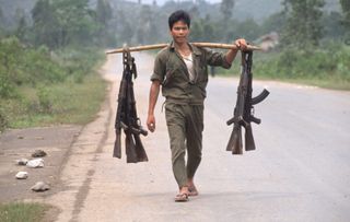 Rifles hang from a stave across a soldier's shoulder. | Location: Dung Ha, Vietnam. (Photo by © Tim Page/CORBIS/Corbis via Getty Images)