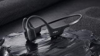The Shokz OpenRun Pro sitting in a pool of water on top of a rolled up black yoga mat.
