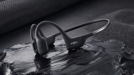 The Shokz OpenRun Pro sitting in a pool of water on top of a rolled up black yoga mat.