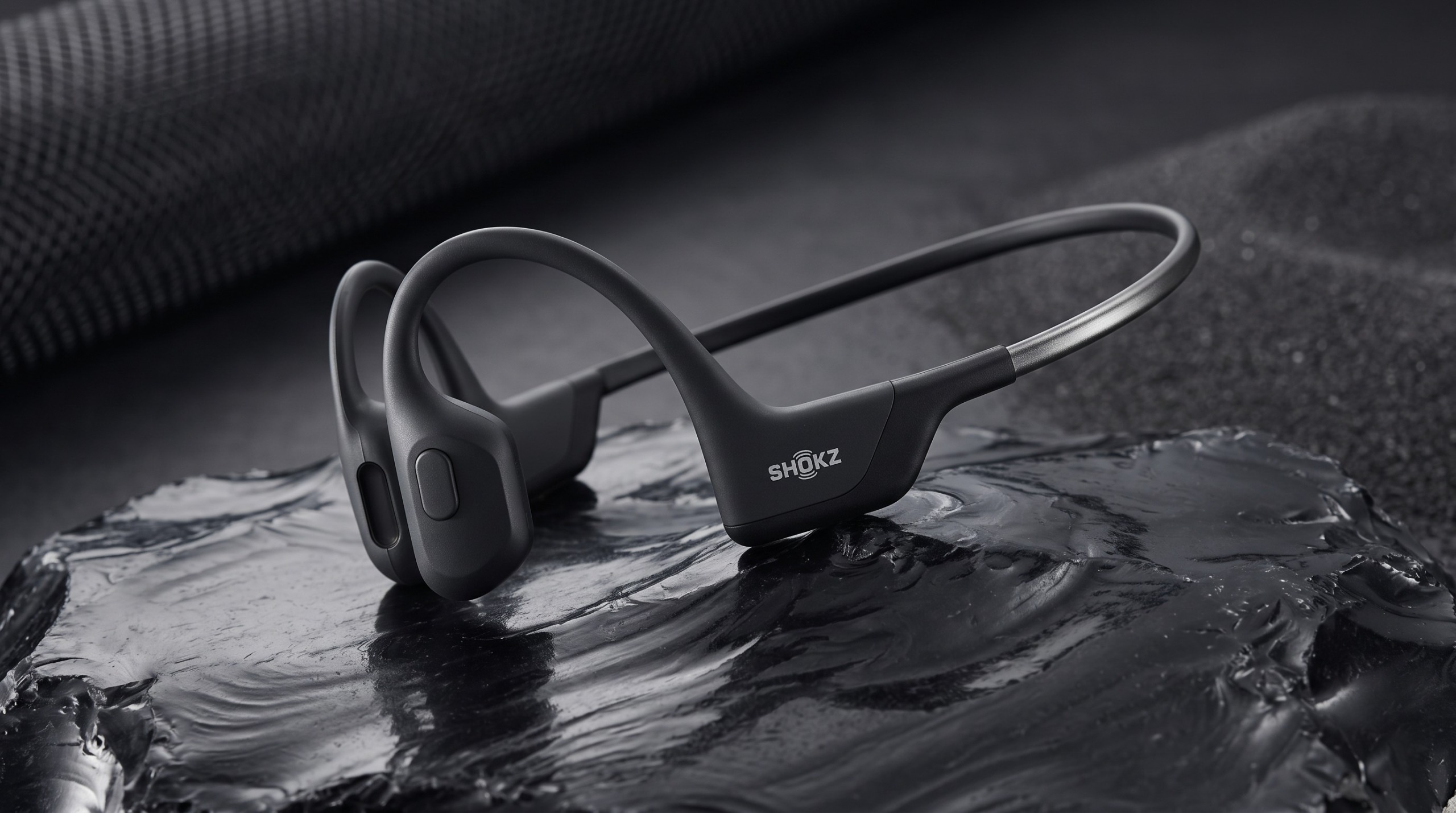 The Shokz OpenRun Pro sitting in a pool of water on top of a rolled up black yoga mat.