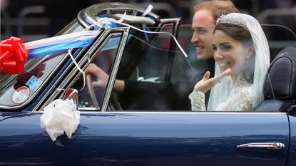 Kate Middleton wearing a gown, veil and tiara sitting in a blue convertible car next to Prince William driving away after their wedding 