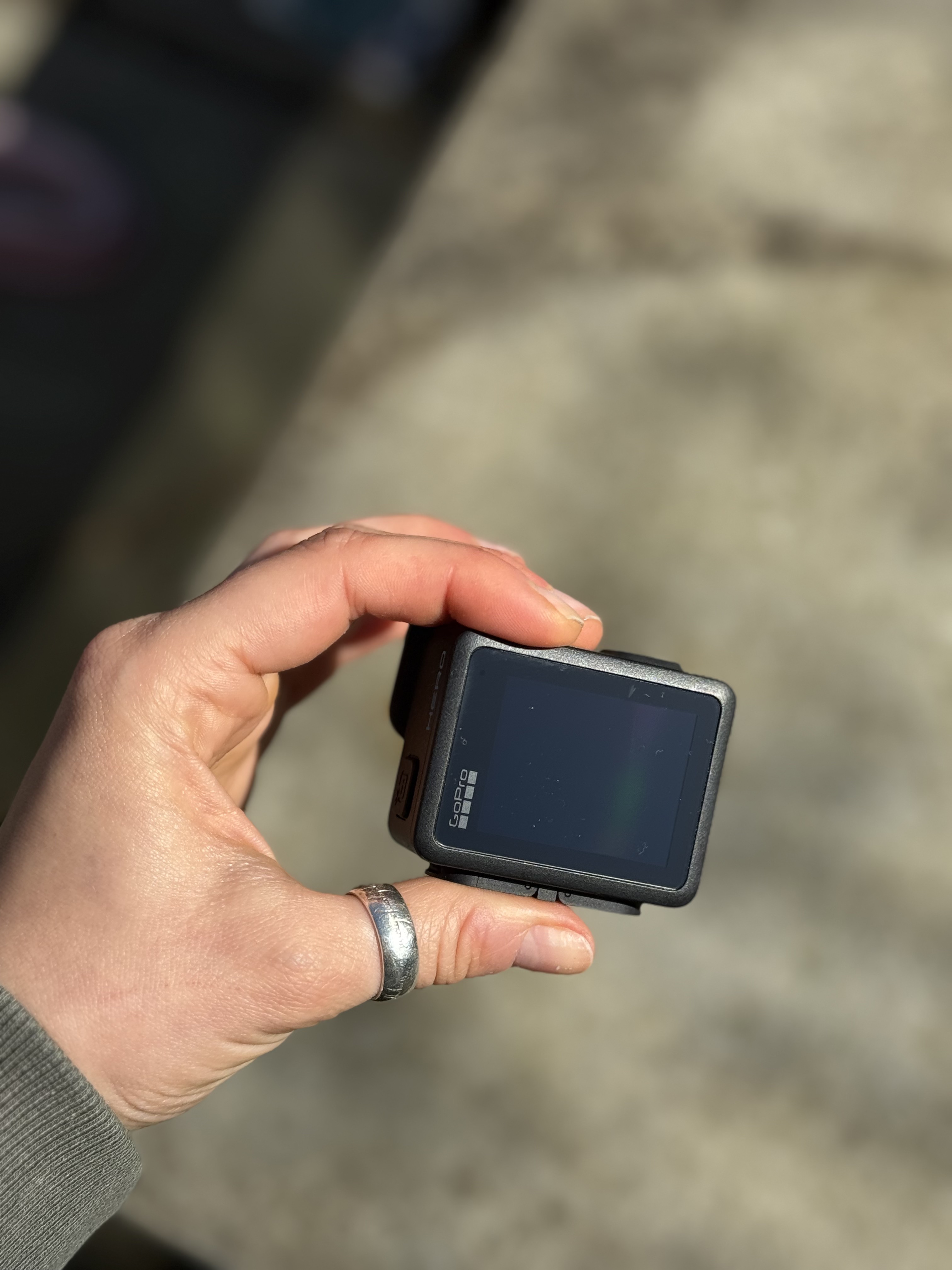 A small black action camera with the screen on. You can see a garden and picnic blanket in the viewfinder