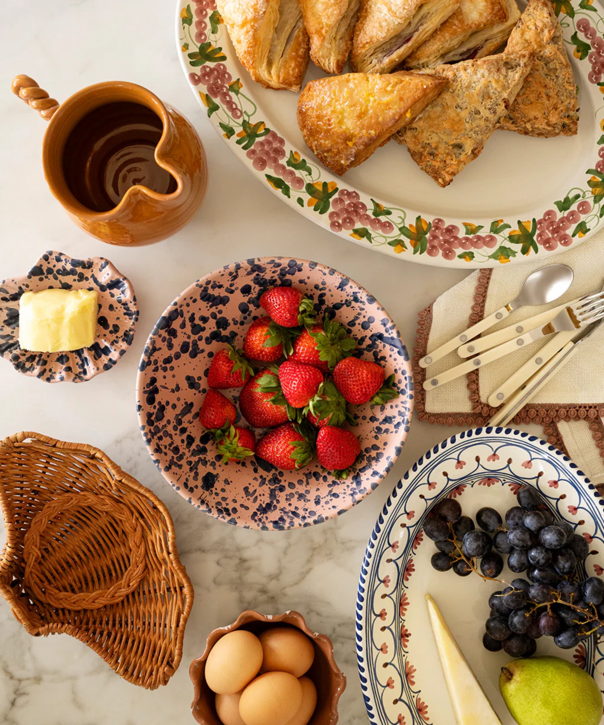tablescape on a marble kitchen island styled with vintage inspired floral painted platters and splattered bowls with a rattan shell shaped bowl