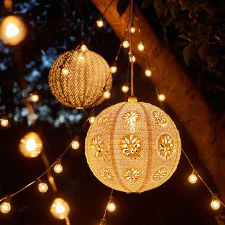 Two lace pendant lantern lights hanging from tree branch at night