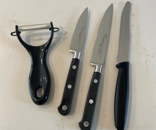 Black plastic utensils (a peeler, two chef knives and a bread knife)