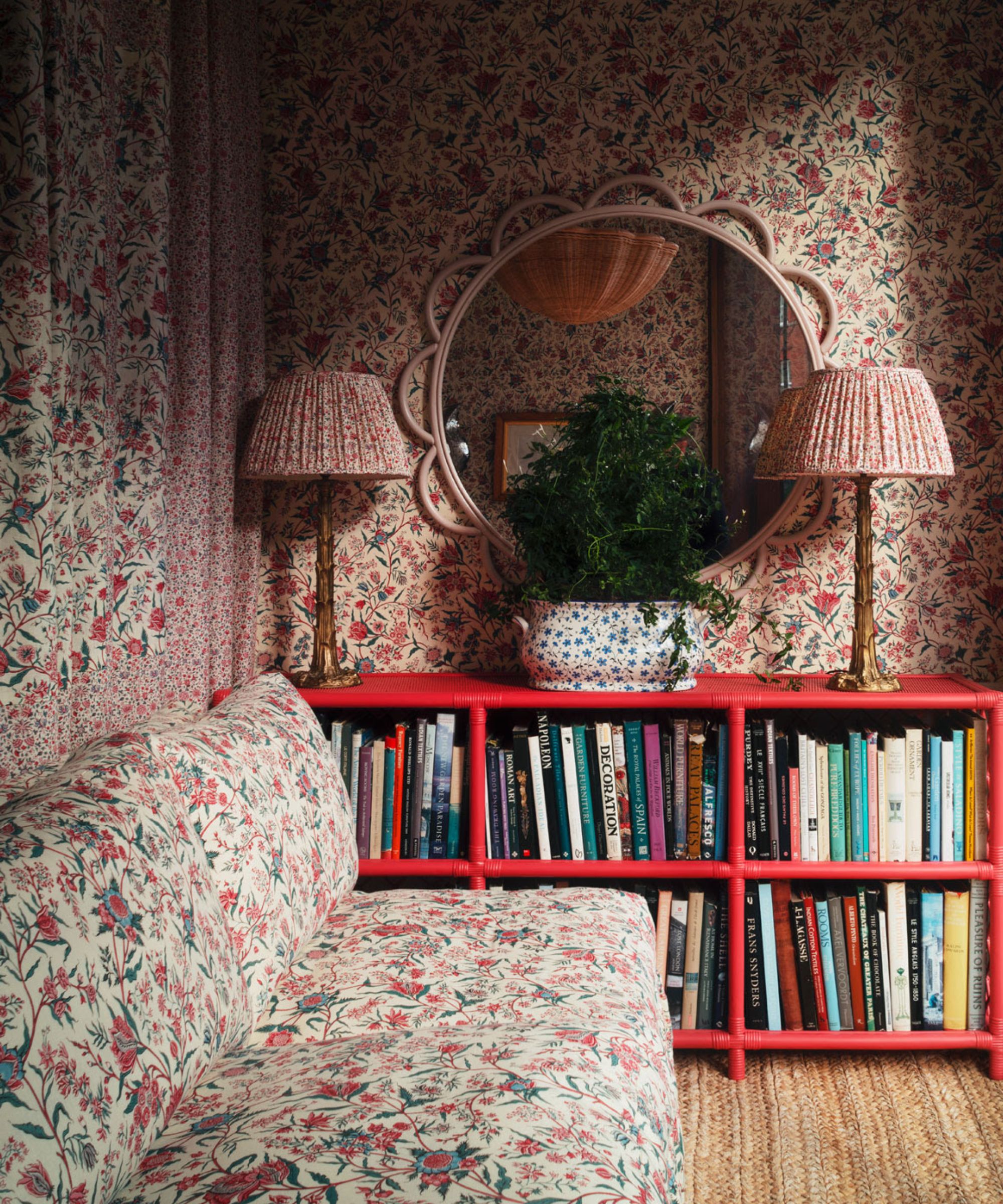 Pink and red living room with floral wallpaper and fabric, red book shelf, two matching lamps