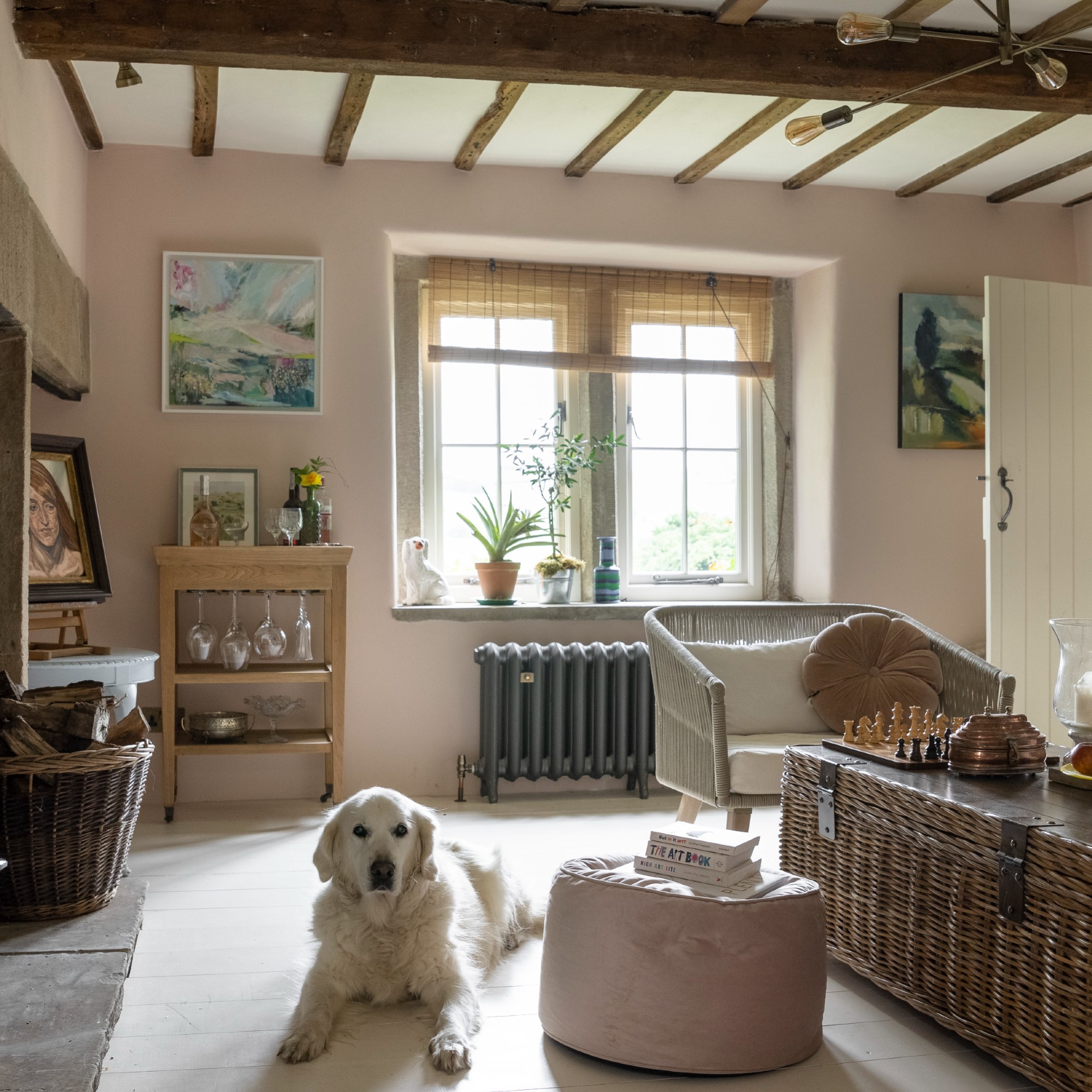 A pink-painted living room with a storage coffee table and bamboo roller blinds dressing the window